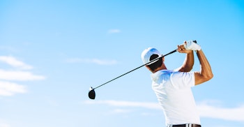 A man in a white golf shirt swinging a club against a blue sky
